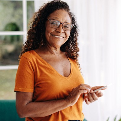 Senior woman with glasses smiling while looking at phone
