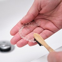 Patient using toothbrush to clean aligners in sink