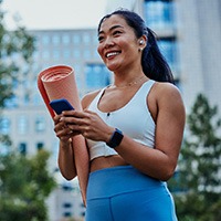 Smiling woman walking on park with workout mat