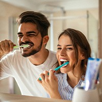 Couple smiling while brushing teeth in bathroom