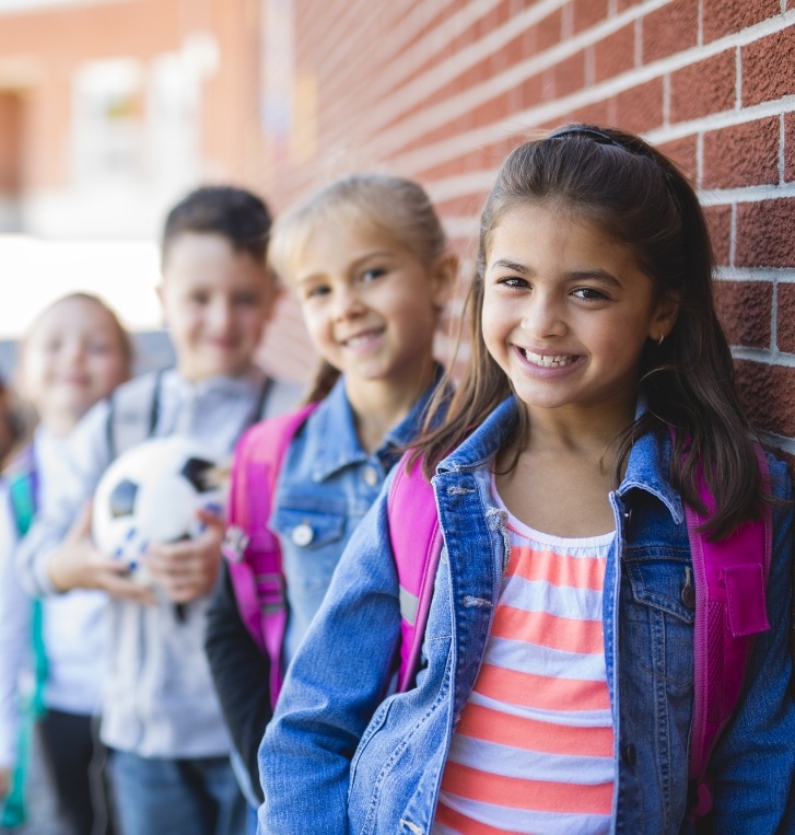 Group of kids with backpacks smiling against red brick wall