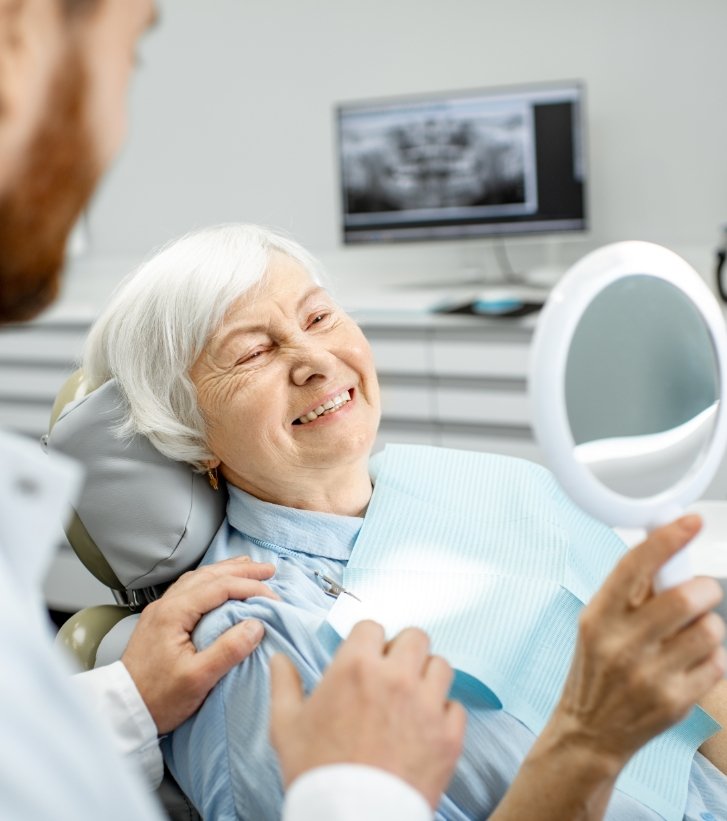 Senior dental patient admiring her smile in mirror
