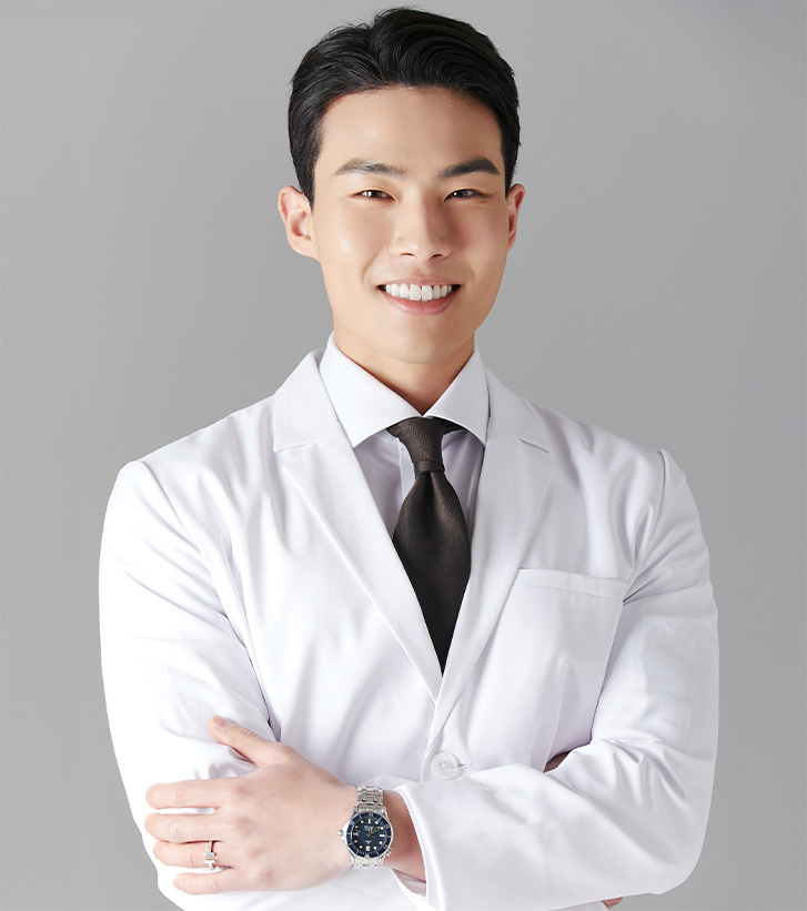 Dr. Marcus Hwang wearing a white coat and black tie smiling in front of a gray background.