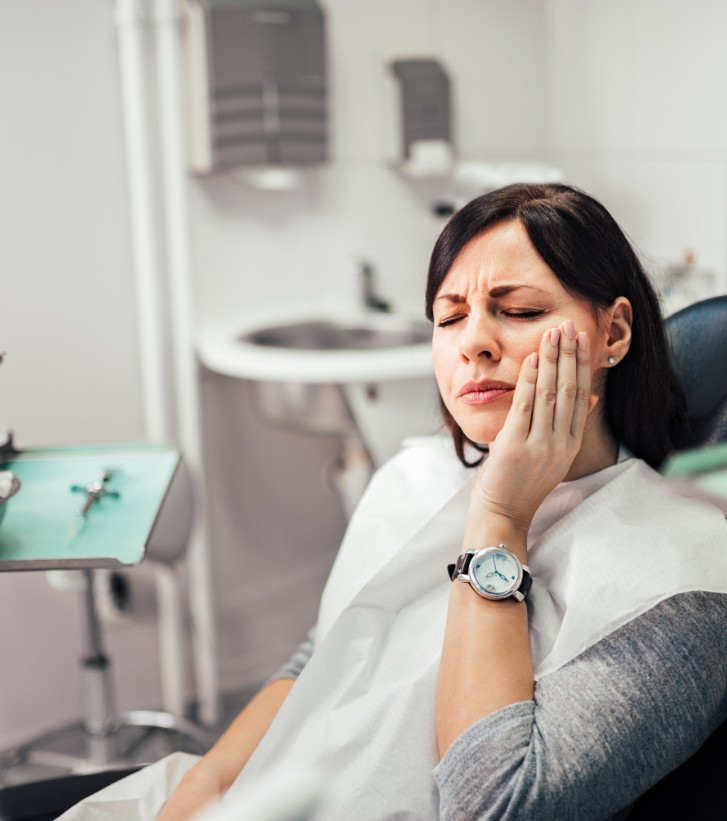 Woman in dental chair holding her cheek in pain