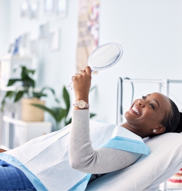 Woman admiring her smile in a mirror while visiting dentist in Beaverton