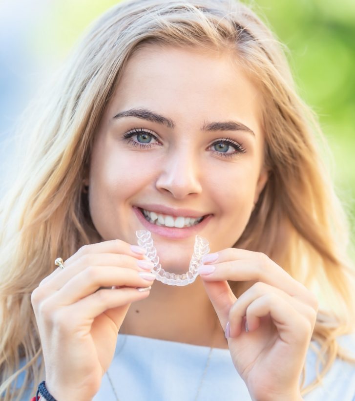 Young blonde woman holding an Invisalign aligner