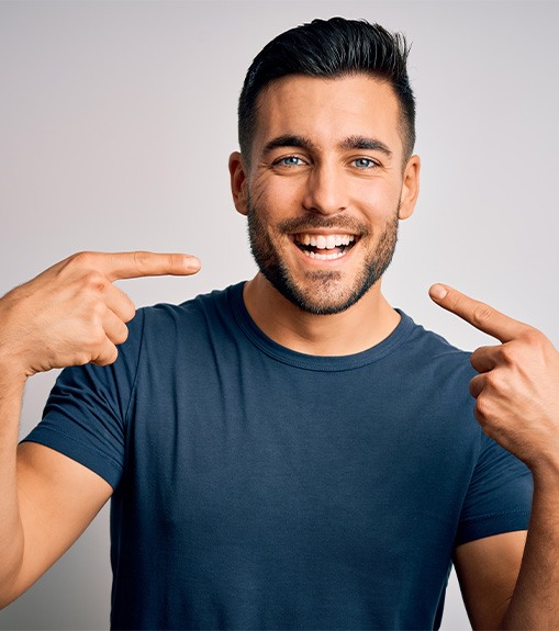 Man in blue shirt pointing to his face with both hands