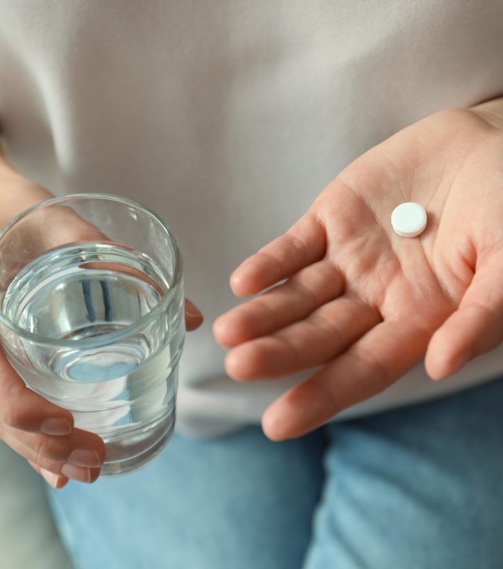 Person holding glass of water and white pill