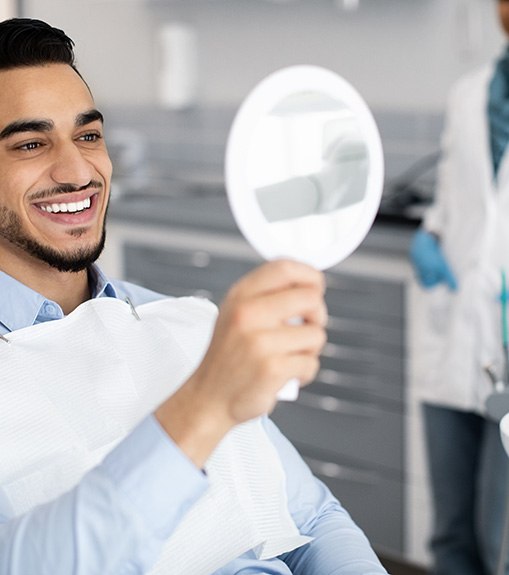 Man in dental chair admiring smile in handheld mirror