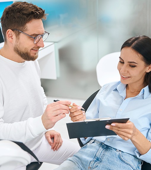 Woman in dental chair filling out forms for dentist wearing white